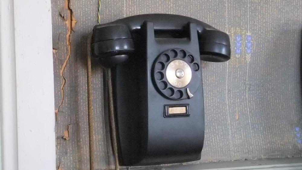 En gammal svart telefon som hänger på väggen.